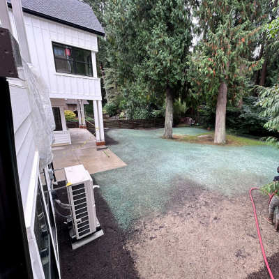 Hydroseeding lawn process beside residential home with a worker operating equipment.
