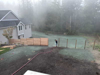 Person with hose watering new grass in backyard of house on foggy day.