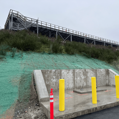 Hydroseeding process on slope with wooden staircase and concrete structure in foreground.