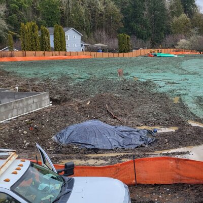 Construction site with machinery, hydroseeding, and orange safety fencing.