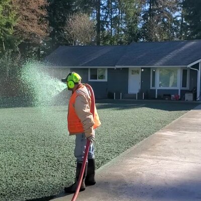 Worker spraying liquid on lawn near residential home.