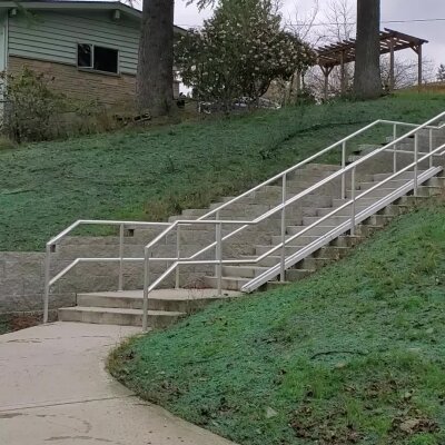 Outdoor staircase with handrails on a grassy hill, residential area.