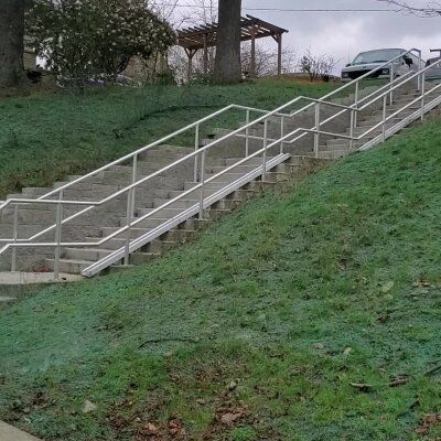 Outdoor concrete staircase with metal handrails on grassy hill.