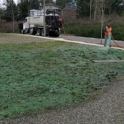 Worker hydroseeding lawn with machinery, residential area.