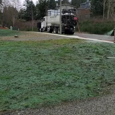 Truck on a street spraying green hydroseed on soil.
