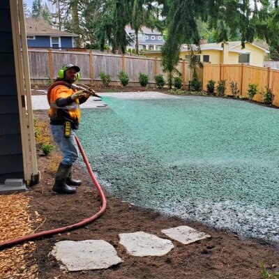 Worker spraying grass seed hydroseeding in residential backyard.