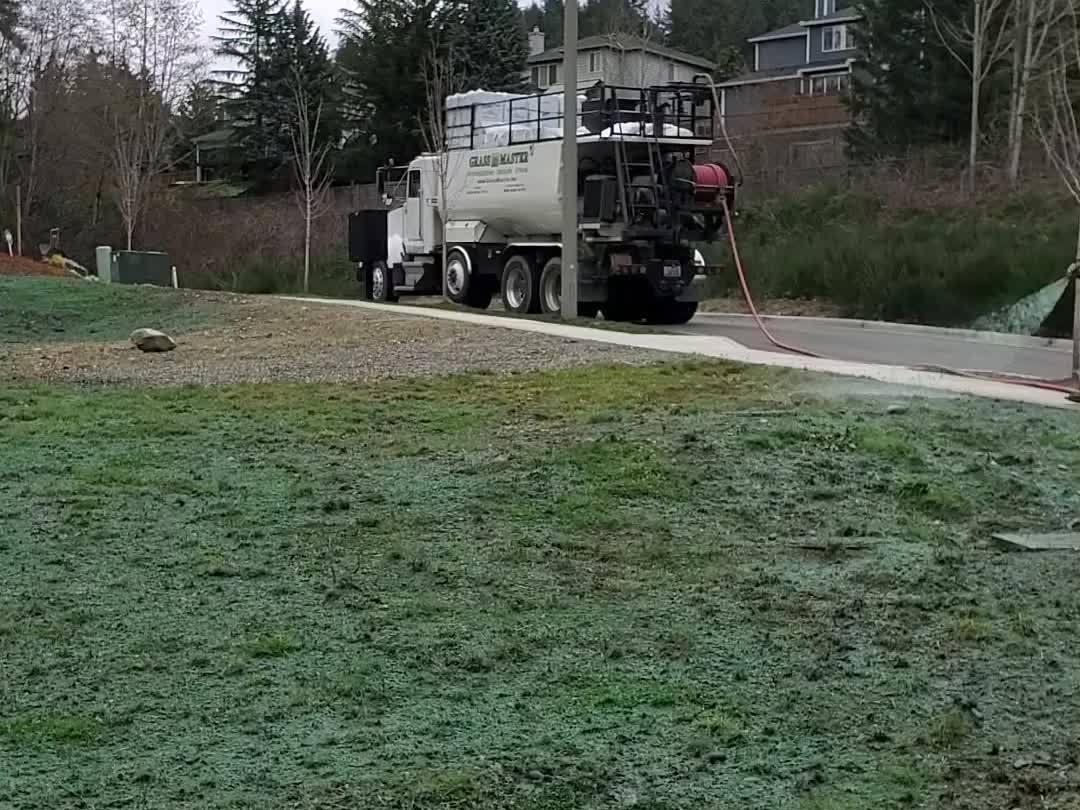 White Grass Master truck on a driveway with a terraced hillside, stone retaining walls, and homes behind