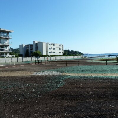 Urban development area with buildings, prepared soil, and water view in the background.