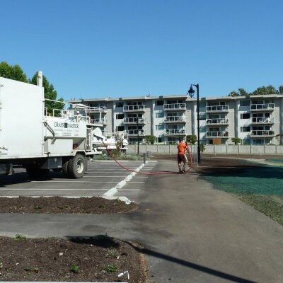 Worker using hydroseeding equipment near apartment buildings.