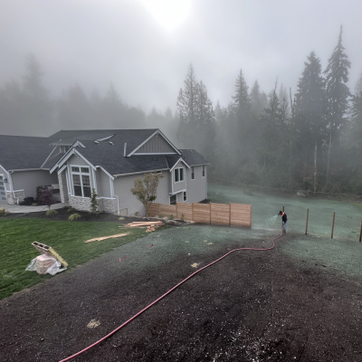 House and garden in foggy landscape with person watering grass.