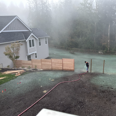 Person with hose watering new grass in backyard of house on foggy day.