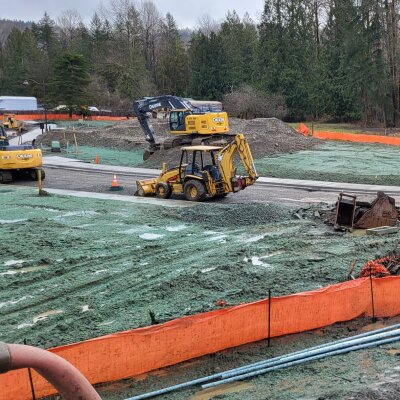 Construction site with heavy machinery and hydroseeding in progress.