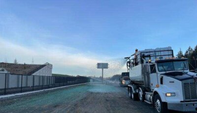 Semi truck spraying water on construction site road at dusk.