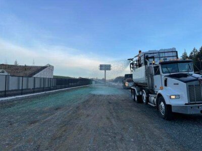 Semi truck spraying water on construction site road at dusk.