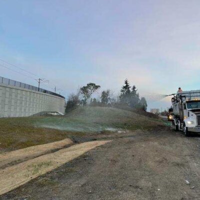 Truck spraying water on grass by the roadside near a concrete wall.