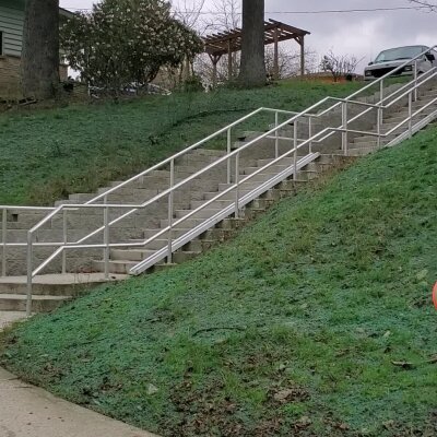 Outdoor staircase with railing on grassy hillside, car and gazebo in background.