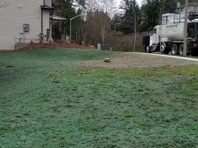 Grassy field with a cement truck and building in the background.