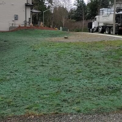 Grassy field with a cement truck and building in the background.