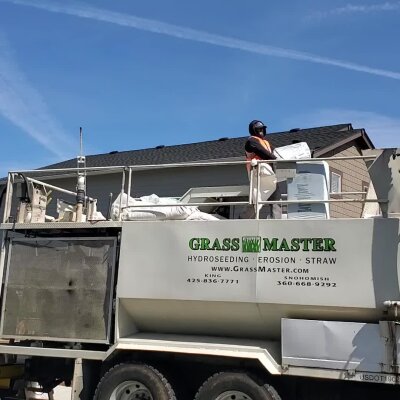 Worker loading material into hydroseeding truck near residential building.