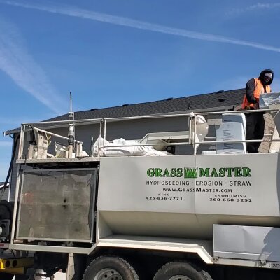 Worker standing on hydroseeding truck outside residential home.