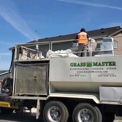 Worker on hydroseeding truck with equipment, sunny day.