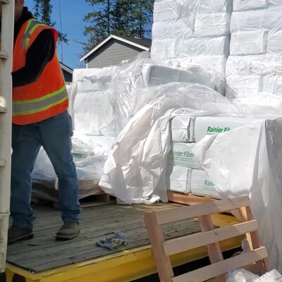 Worker in safety vest unloading insulation material from truck.