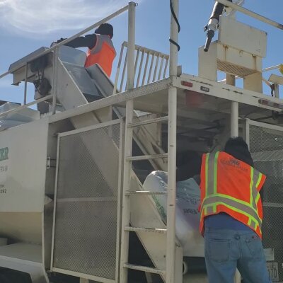 Workers in high-visibility vests loading material into truck.