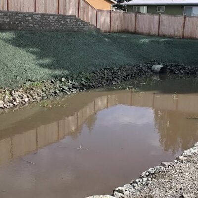 Small pond with culvert under fence in suburban area.