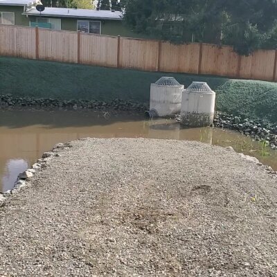 Backyard with flood prevention infrastructure, rock-lined water pooled area, wooden fence.