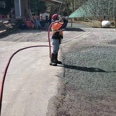 Worker spraying water on gravel road with hose.