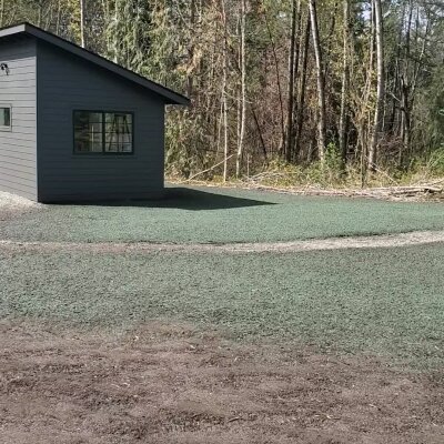 Small gray house with surrounding green area and forest in the background.