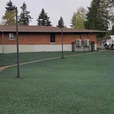 Grassy area with light poles in front of a brick building with HVAC units.