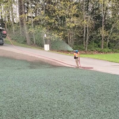 Person working with hose on artificial turf near trees.