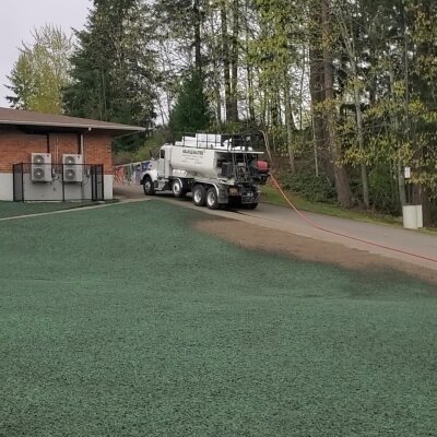 Tanker truck on green surface near trees and building.