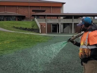 Worker spraying green hydroseed mixture on soil for grass growth.