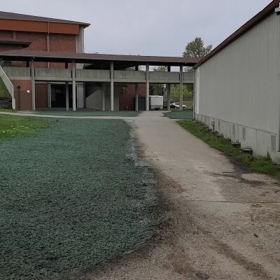 Paved path leading to a modern building with a covered walkway and green lawn.