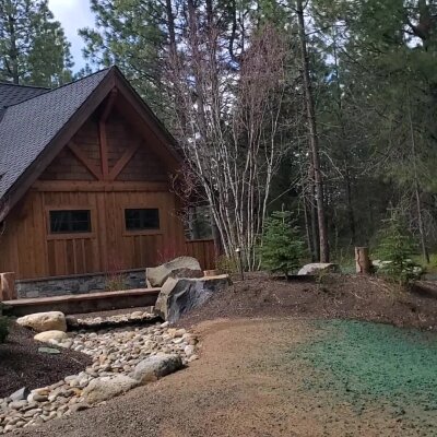 Wooden cabin with stone accents in a forest setting.