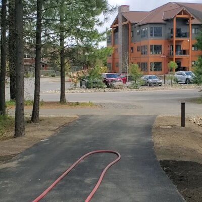 Paved path leading to a multi-story building with trees and parked cars.