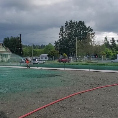 Worker hydroseeding lawn with hose in overcast weather.