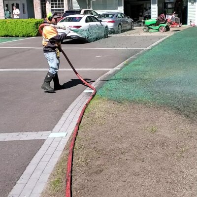 Worker hydroseeding lawn with green slurry near sidewalk.