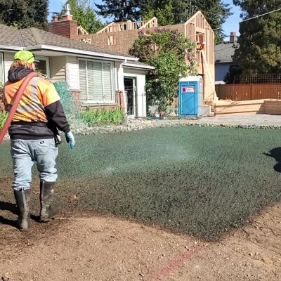 Worker hydroseeding lawn in front of residential home.