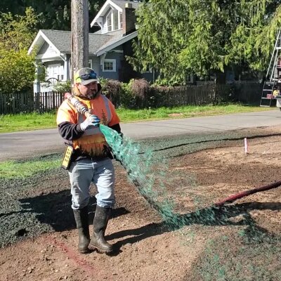 Worker hydroseeding new lawn in residential area.