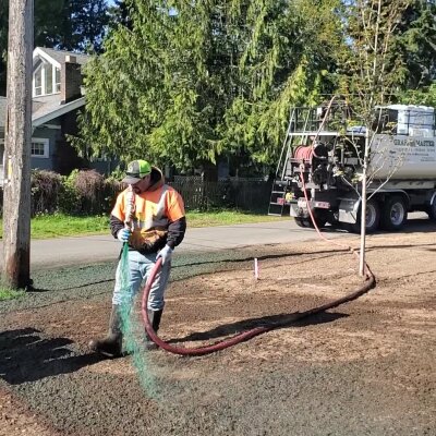 Hydroseeding technician spraying green mixture on lawn in Washington state.