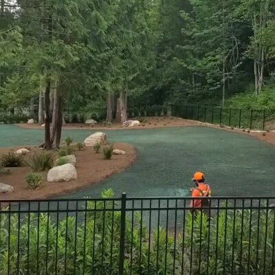 Hydroseed installation in wooded residential backyard with worker in bright safety gear.