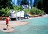 Worker applying hydroseed with hose from truck near residential area.